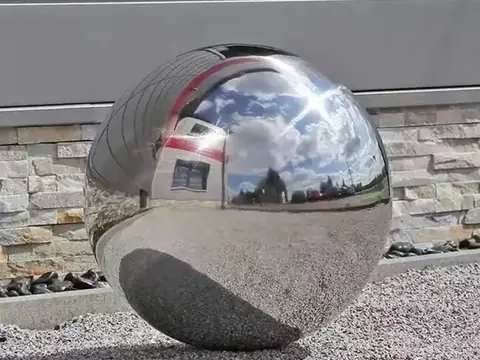 A large, polished stainless steel sphere reflecting the sky and building exterior.