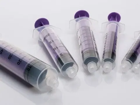 Various sizes of plastic medical syringes with purple plungers on a white reflective surface