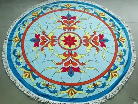 Round blue beach towel with colorful floral mandala print and white fringe, laid flat on a concrete floor