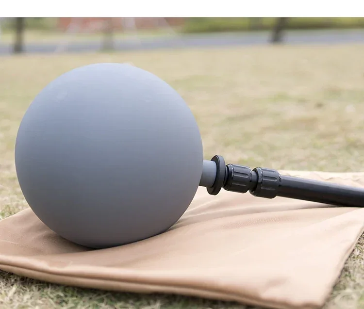 Gray ball-shaped device with a black handle resting on a tan fabric pouch on grass outdoors