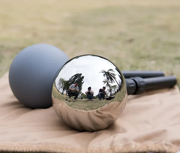 A polished chrome sphere and a matte gray sphere resting on beige fabric outdoors