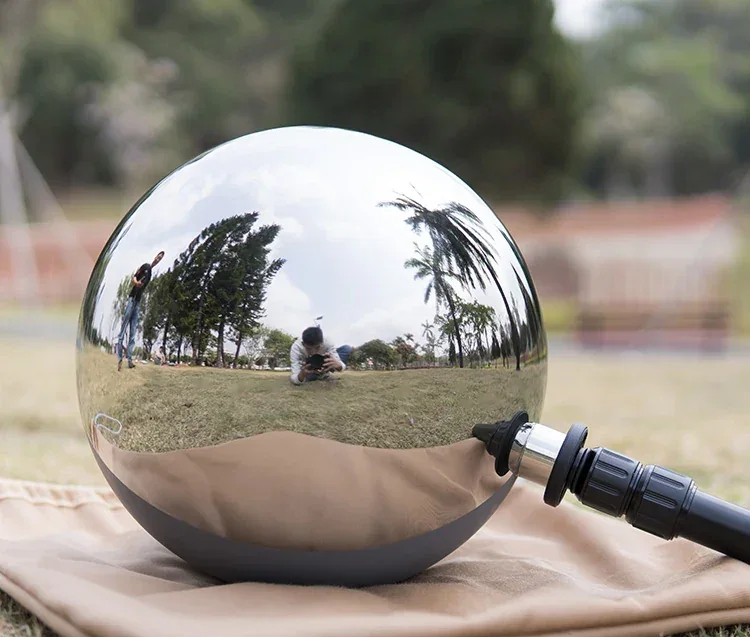 A highly polished, reflective stainless steel sphere resting on a cloth outdoors.