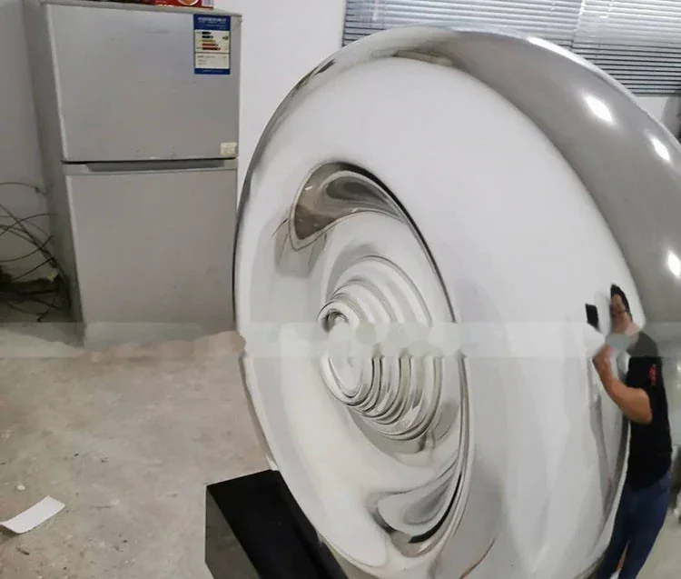 A large, polished stainless steel sculpture with a swirling, concave center.