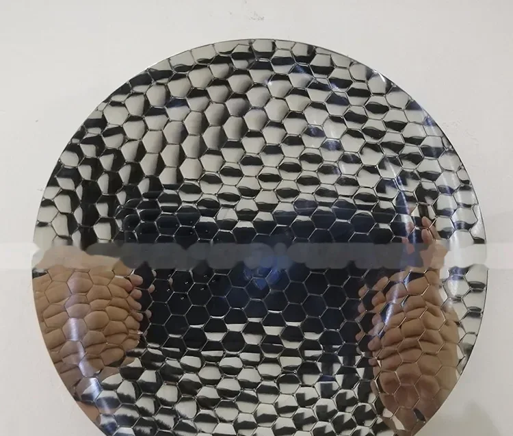 Circular mirror-finish plate with embossed hexagonal honeycomb texture held up against a plain wall