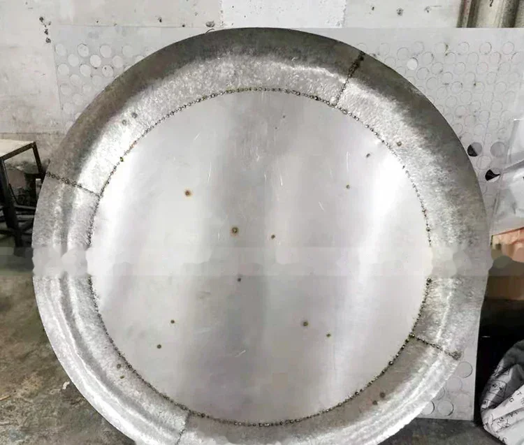 Large circular steel dished tank head with visible weld seams standing in an industrial workshop
