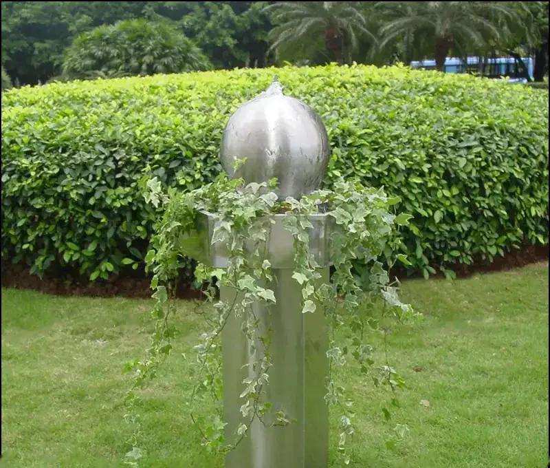 Edelstahlkugel Wasserspiel mit nachlaufendem Efeu auf einem Metallsockel in einem grasbewachsenen Garten