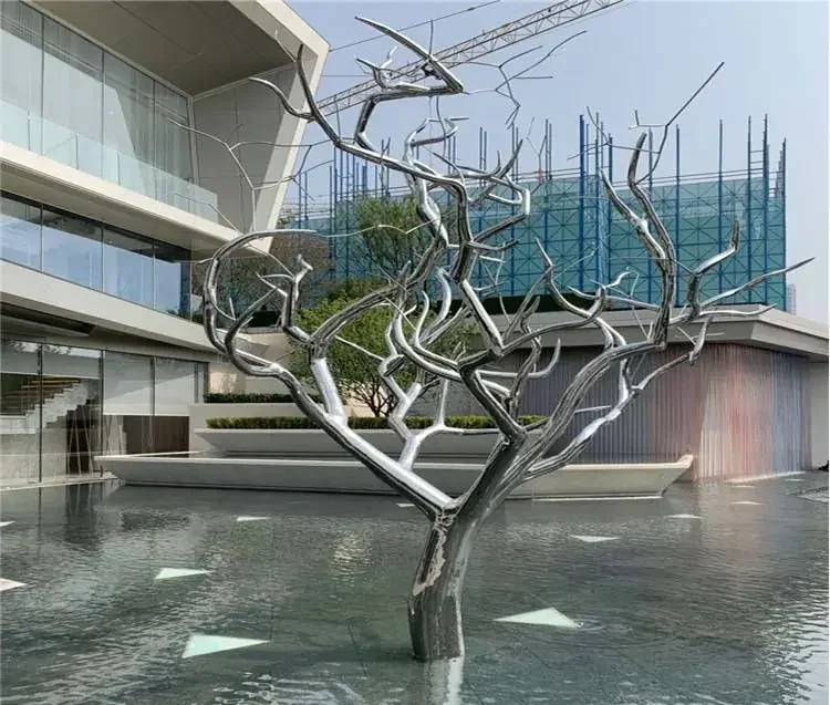 Polished stainless steel tree sculpture installed in a reflecting pool outside a modern building