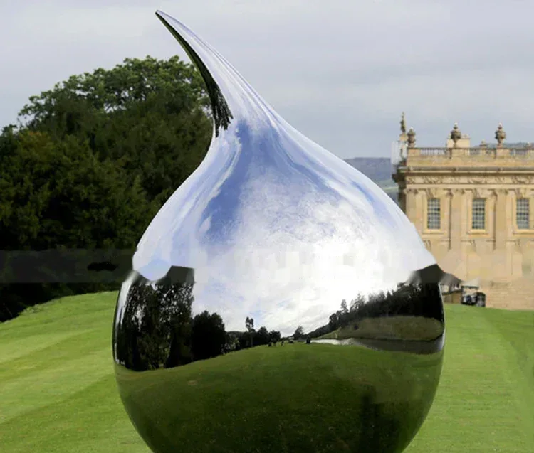 Reflective silver teardrop sculpture on a lawn in front of a large stately home