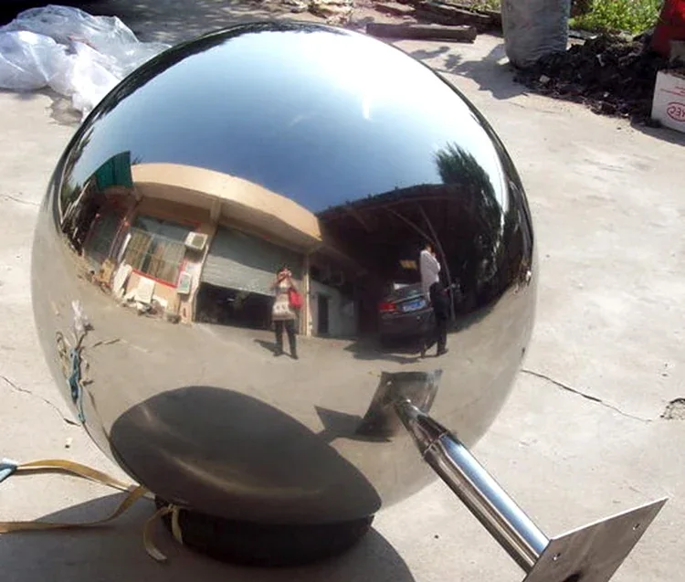 Polished stainless steel sphere on a cylindrical post photographed outdoors on a concrete surface