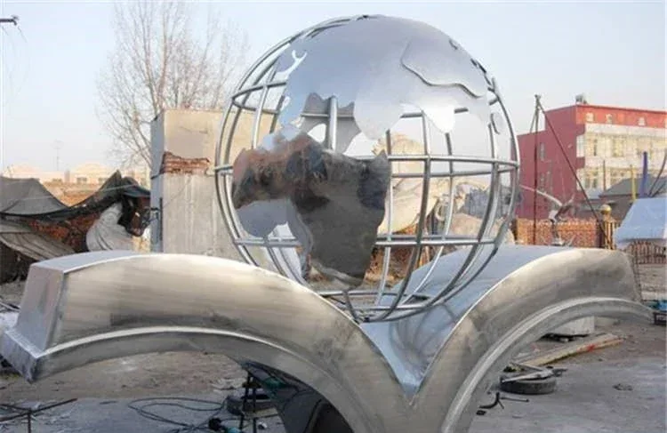 Escultura de acero inoxidable pulido en una base de libro abierta en un patio de fabricación al aire libre