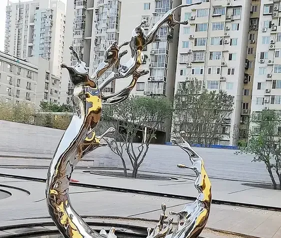 Large polished stainless steel liquid splash sculpture installed in an outdoor plaza with residential high-rise buildings behind