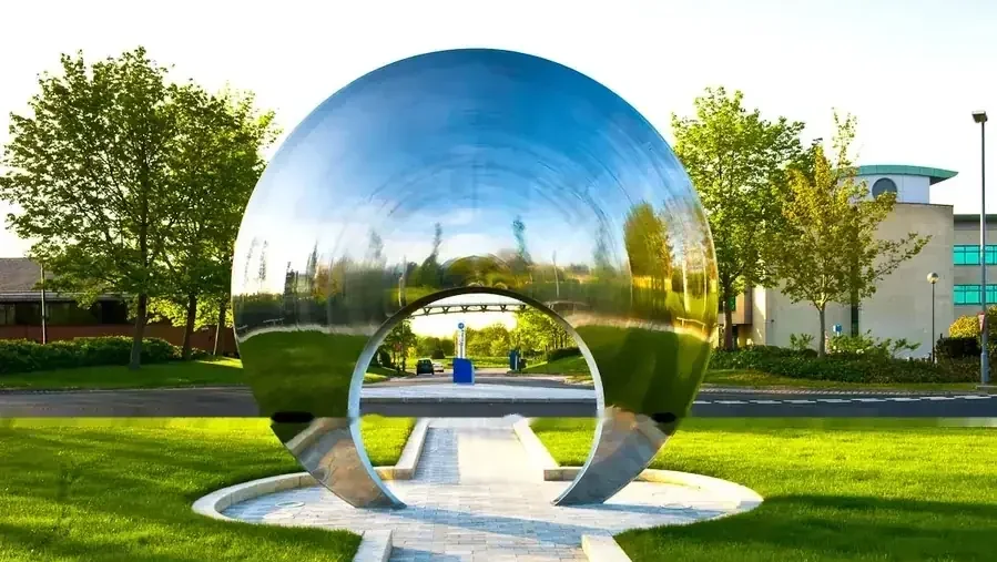 A large, polished metal sphere sculpture with an archway cutout stands on a lawn.