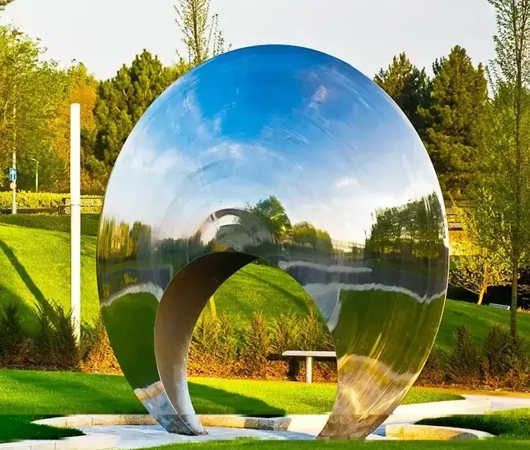 A large, polished stainless steel spherical sculpture reflecting the sky and park landscape.