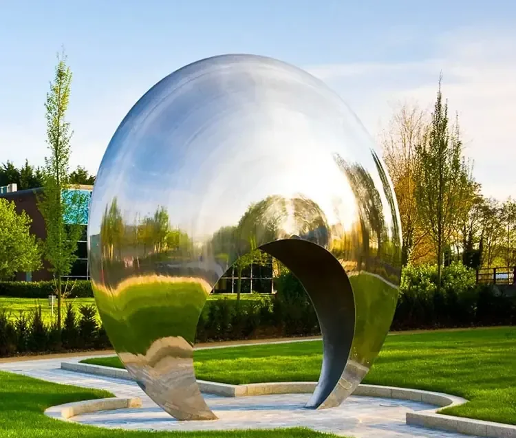 Large polished stainless steel spherical sculpture reflecting a park landscape