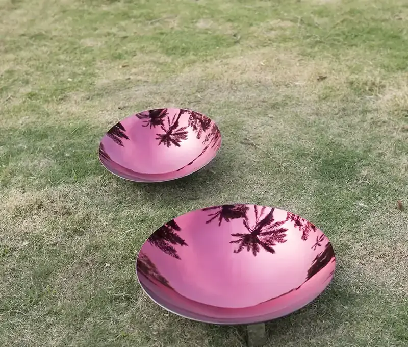 Two pink mirrored discs resting on grass, reflecting trees