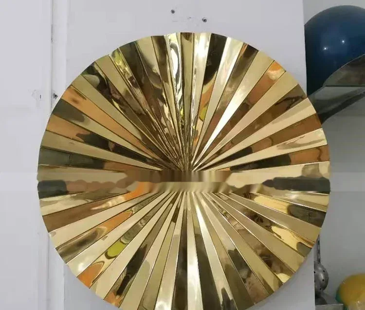 A round, gold-colored metal wall sculpture with a sunburst design.
