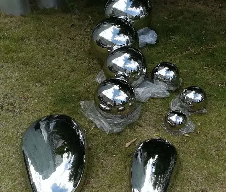 Polished stainless steel spheres in assorted sizes and teardrop shapes arranged on grass with plastic wrap