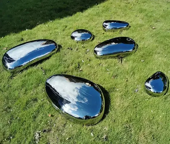 Polished mirror-finish stainless steel pebble sculptures of various sizes arranged on a green lawn