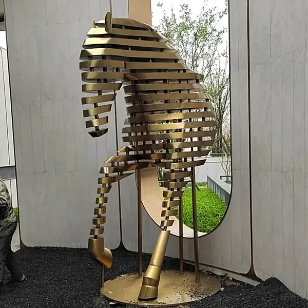 Large golden metal horse sculpture made of horizontal slats, shown outdoors on a round base near a circular window