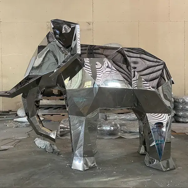 Large polished stainless steel geometric elephant sculpture standing in a metal fabrication workshop