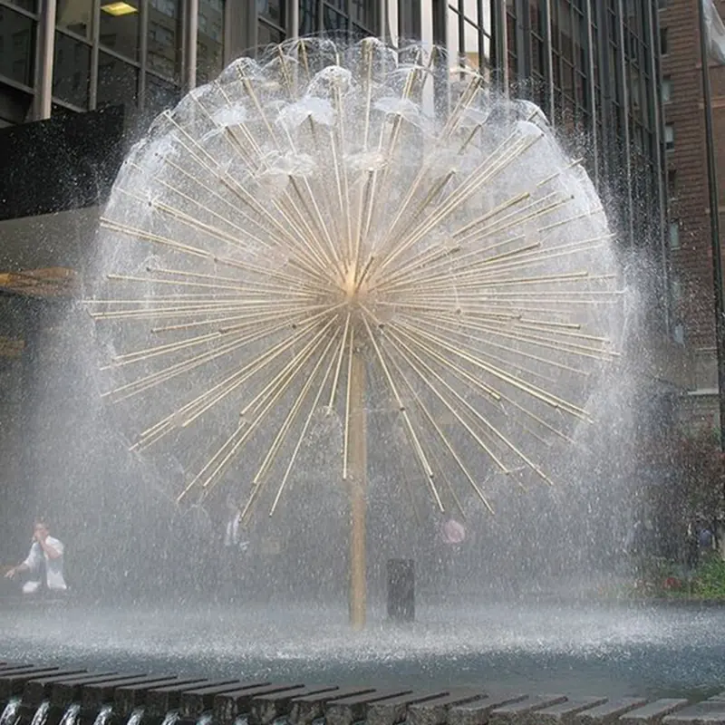 Spherical dandelion-style fountain with radiating golden pipes spraying water in a city plaza surrounded by tall buildings