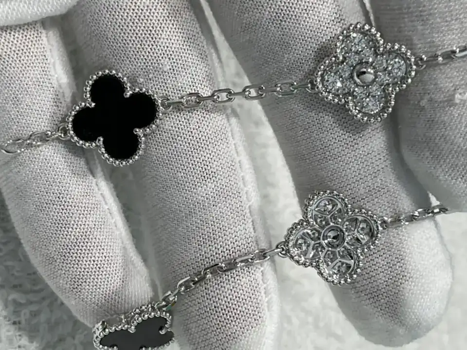 A five motif clover bracelet in onyx and diamond held on a white cloth at BH Jewelry