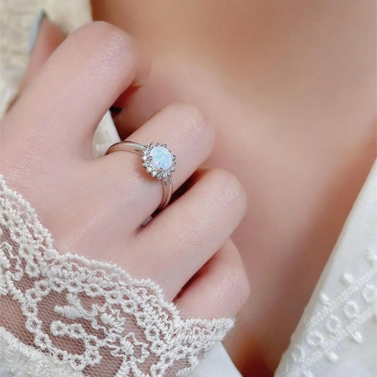 Opal and cubic zirconia ring worn on a hand resting on lace