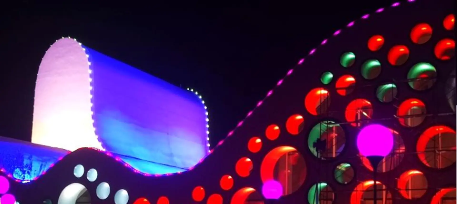 Fachada curva da galeria de arte coberta com pontos redondos de pixels de LED coloridos à noite