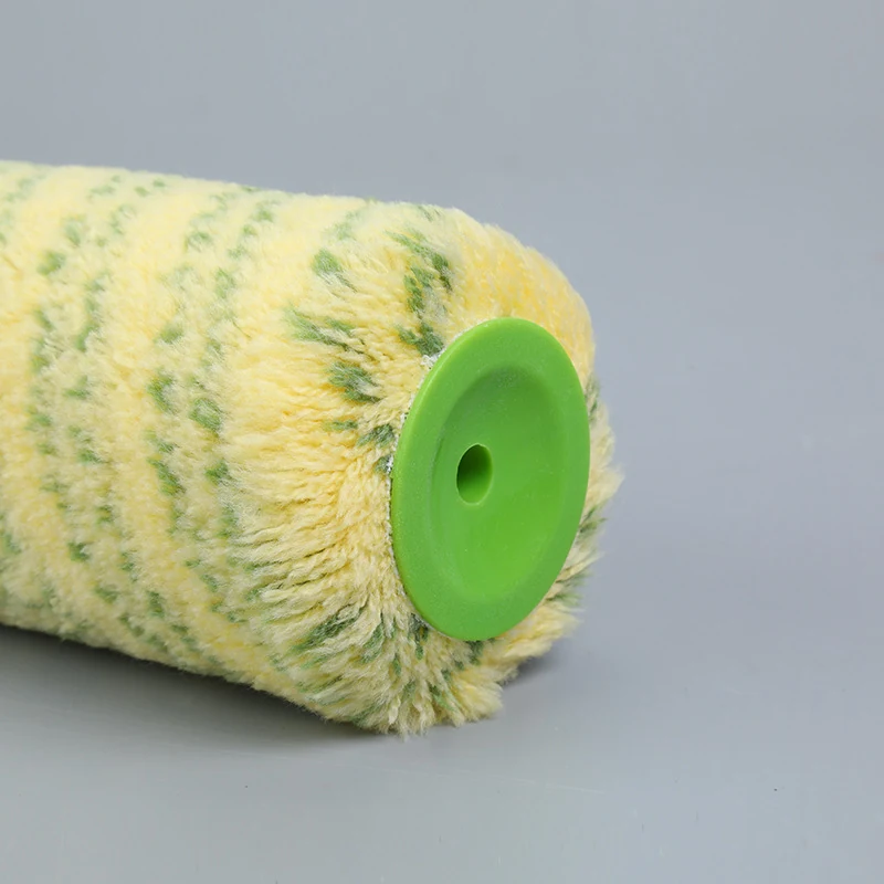 Close-up of a yellow paint roller sleeve with green stripes and a green plastic end cap on a grey background.