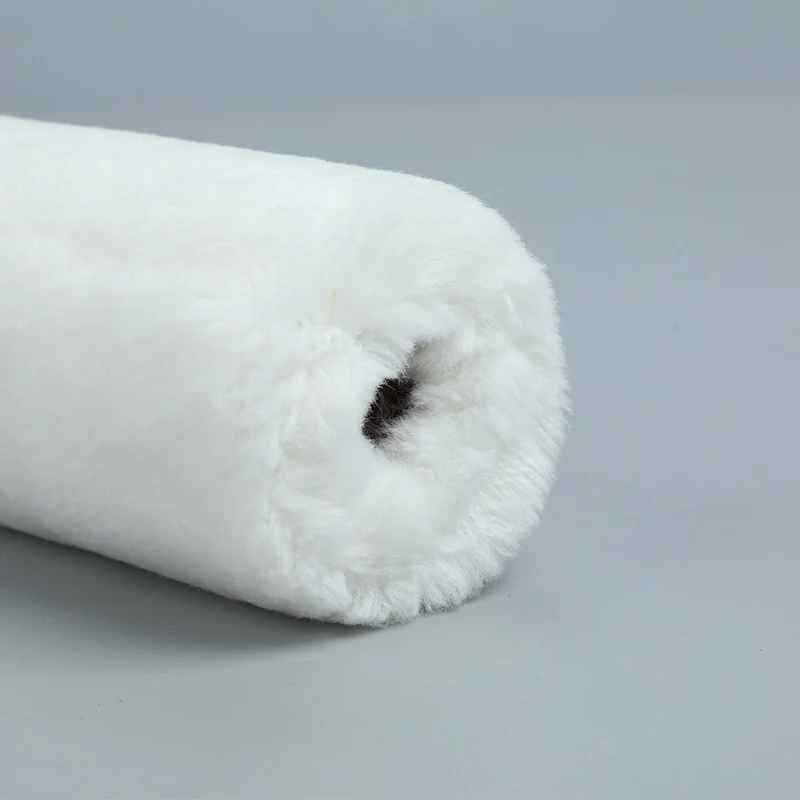 Close-up of a white fluffy fibrous roller sleeve lying diagonally on a plain gray background