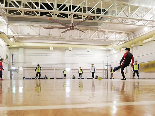 Pavilhão esportivo coberto com ventiladores de teto HVLS acima de uma sessão de futebol infantil
