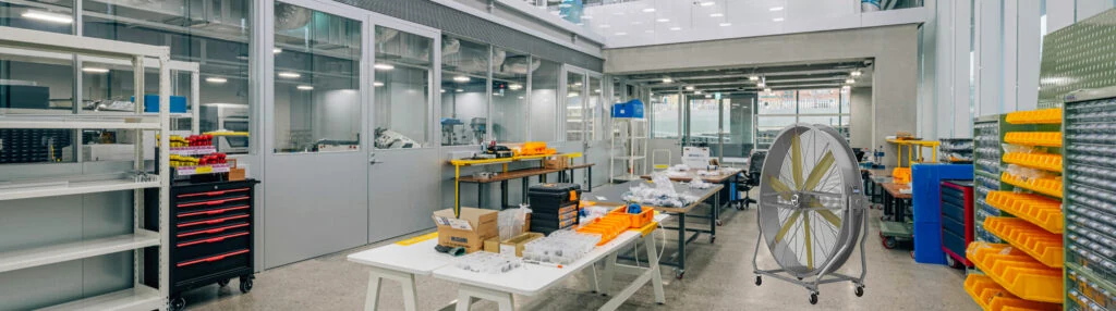 Grande ventilador de piso móvel HVLS fotografado contra um fundo industrial simples