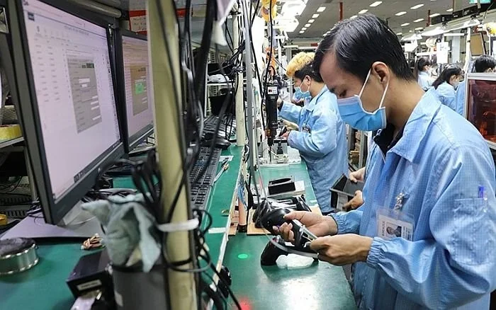 Workers in blue uniforms and masks assemble electronics on a factory production line.