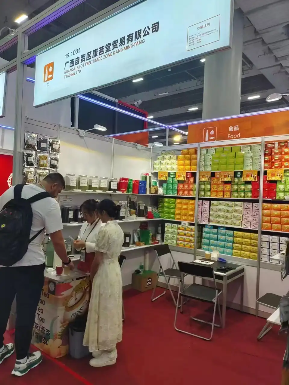 Trade fair booth with shelves of colorful packaged food products and visitors browsing