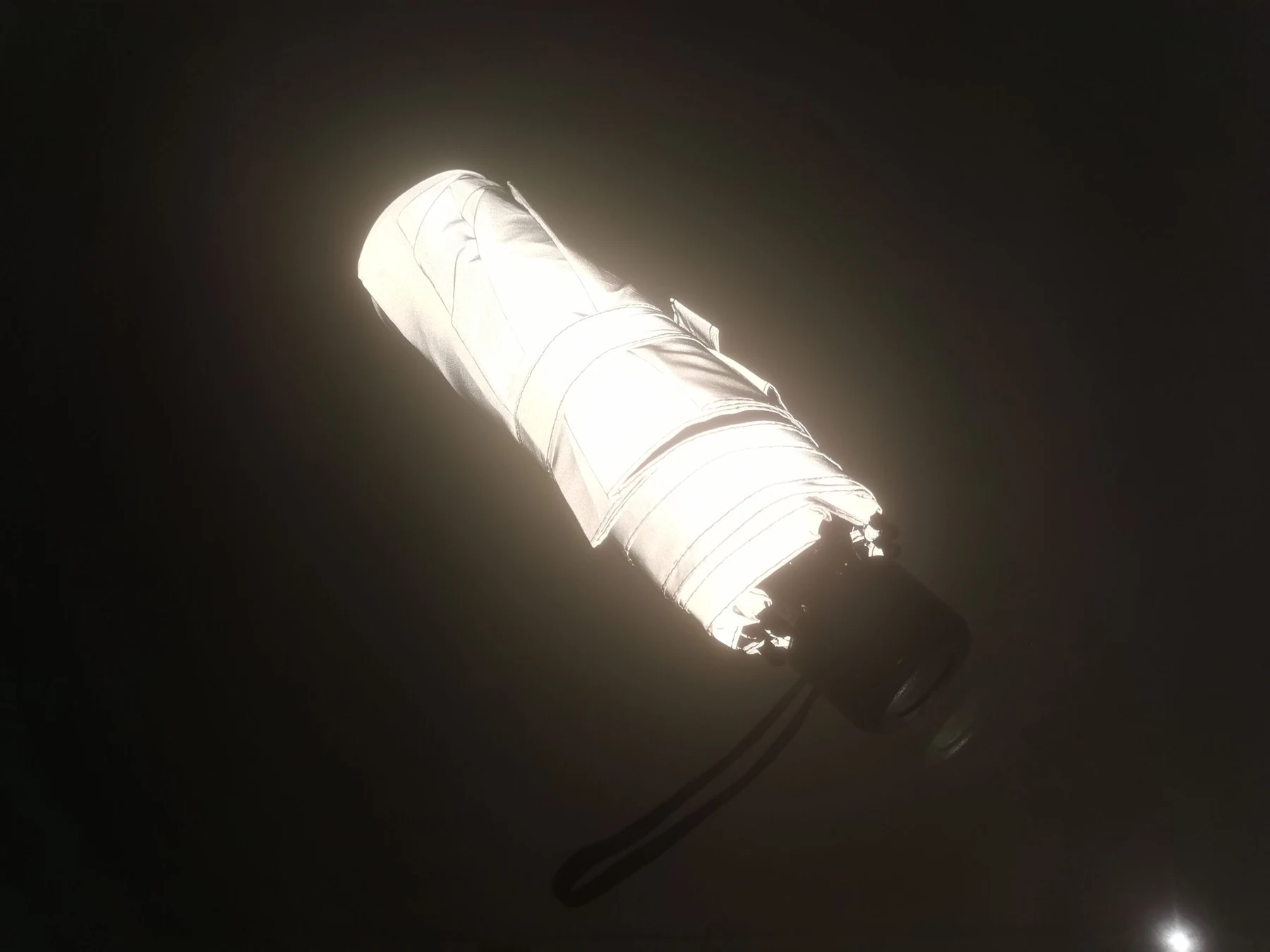 Geschlossener reflektierender Taschenschirm, der in einem dunklen Raum Licht zurückwirft