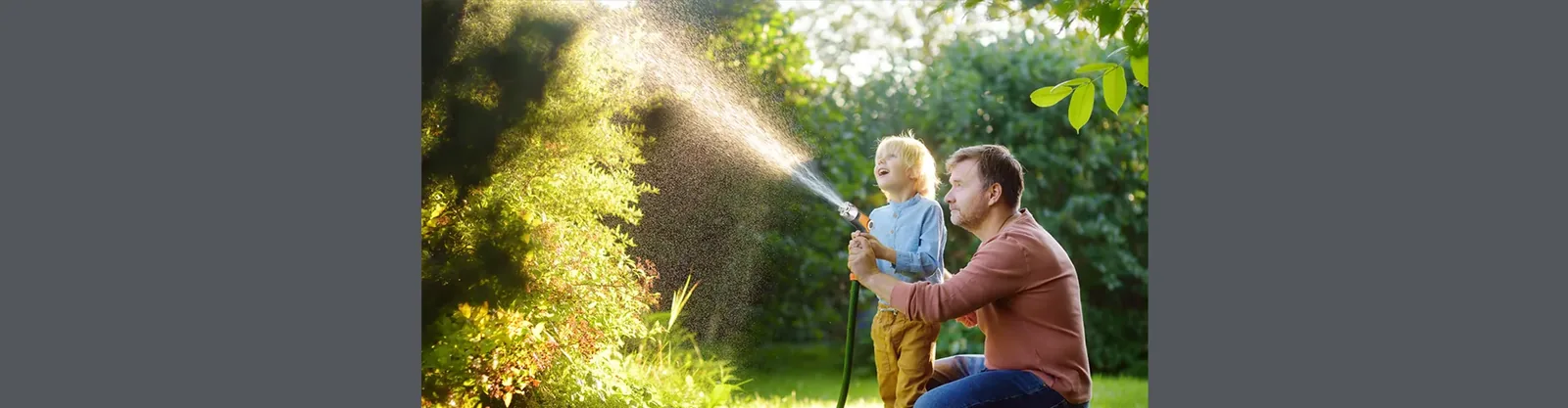 Erwachsener und Kind benutzen eine Gartenspritzpistole auf einem Rasen